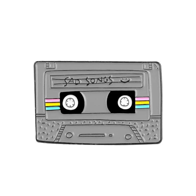A silver enamel pin featuring a cassette tape design with the text SAD SONGS on the label.