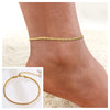 A close-up of a gold-colored snake chain anklet worn on a person's ankle.