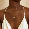 A gold-toned cross pendant necklace is worn around the neck against a dark brown skin tone.