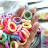 A hand holds a colorful assortment of soft elastic hair bands in various pastel colors like pink, yellow, and purple.