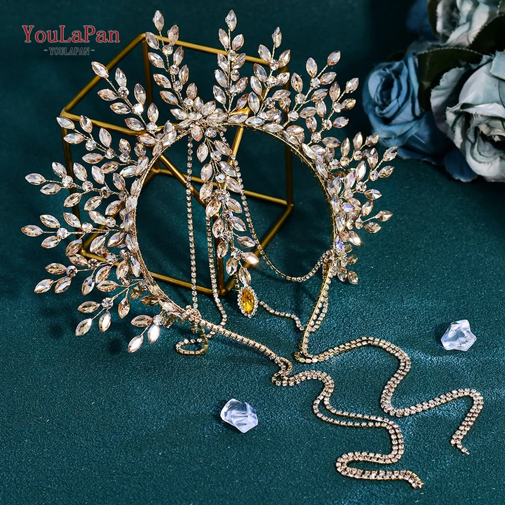A gold rhinestone bridal crown headband with delicate leaves and chains displayed on a dark green velvet background.