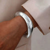 A close-up of a silver cuff bangle bracelet worn on a wrist, next to a light pink fabric.