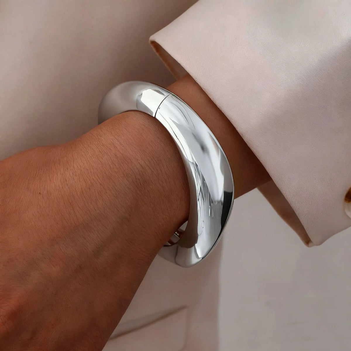 A close-up of a silver cuff bangle bracelet worn on a wrist, next to a light pink fabric.