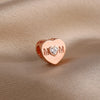 Rose gold heart pendant charm with the initials M M and a diamond center set against a beige fabric background