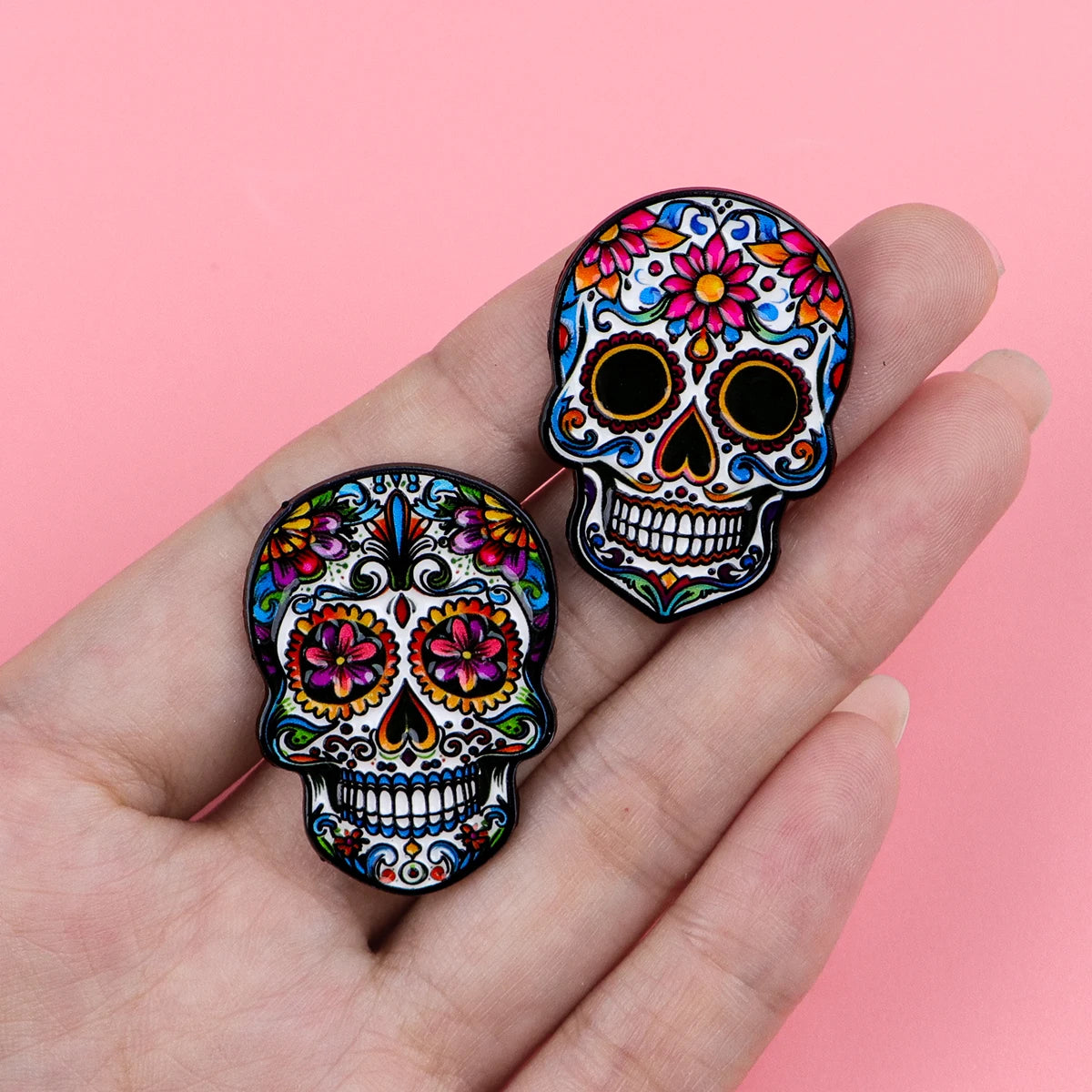 A hand holds a colorful Mexican skull enamel pin brooch featuring intricate floral designs.