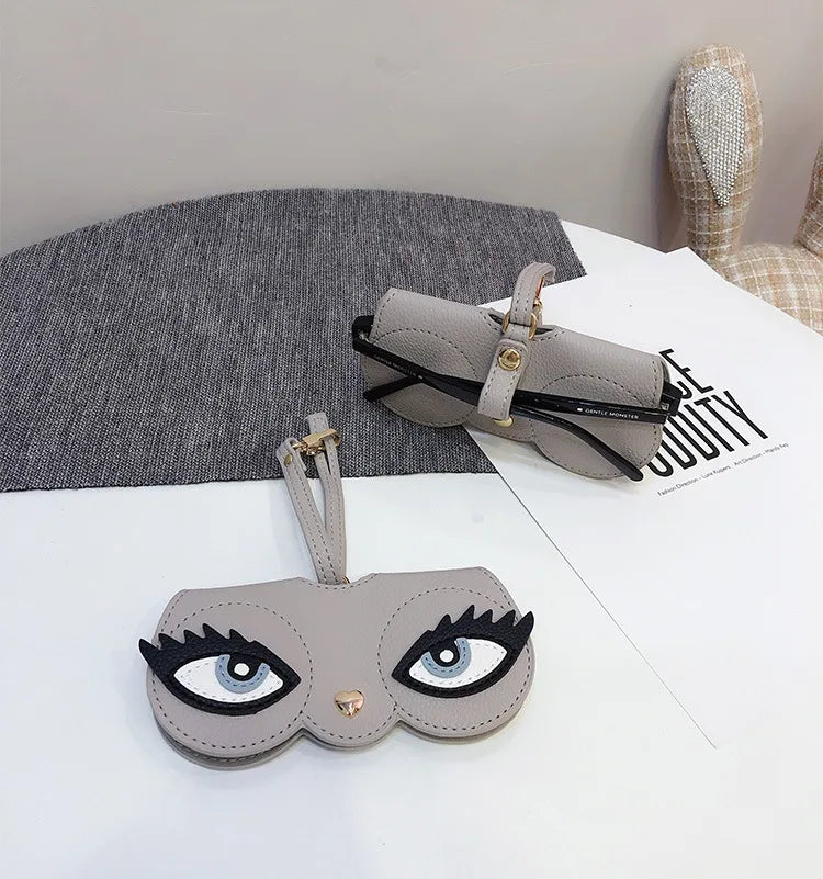 A light gray pouch designed to hold and store a pair of eyeglasses, shown next to a similar-shaped leather accessory.