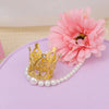 Gold and silver mini crown cake toppers with pearl strands and a pink flower on a purple surface