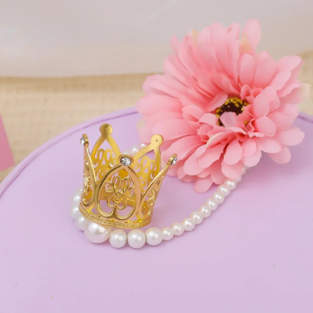 Gold and silver mini crown cake toppers with pearl strands and a pink flower on a purple surface