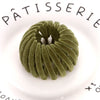 A close-up of a green velvet horsetail hair clip with a spiral design resting on a white plate.