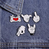 White enamel pins featuring various cartoon finger gestures and a heart on a denim fabric background