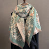 A patterned scarf wrap featuring shades of sage green, beige, and soft orange floral designs draped over a dark garment.