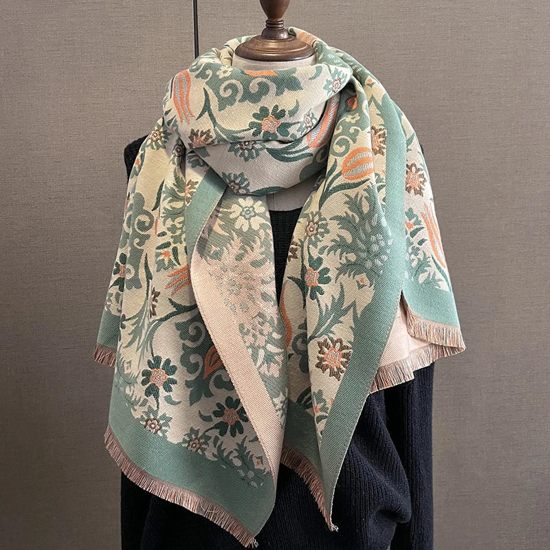 A patterned scarf wrap featuring shades of sage green, beige, and soft orange floral designs draped over a dark garment.