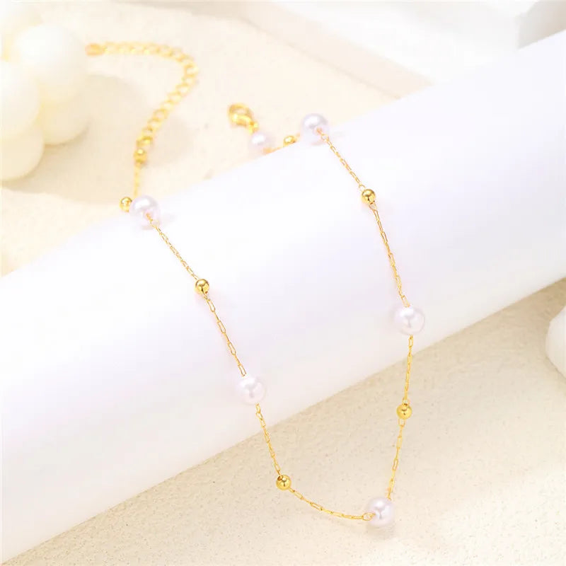 Collier délicat en or avec de petits charms de perles sur fond blanc.