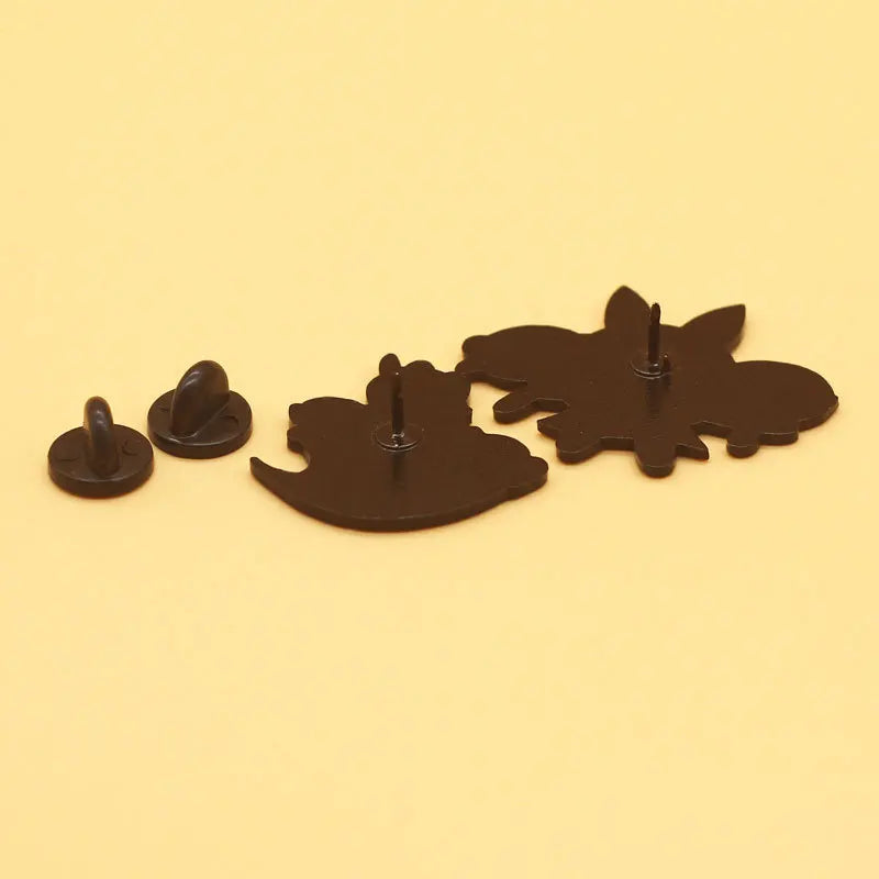 A set of dark brown enamel lapel pins shaped like bats and a bat silhouette on a light background.