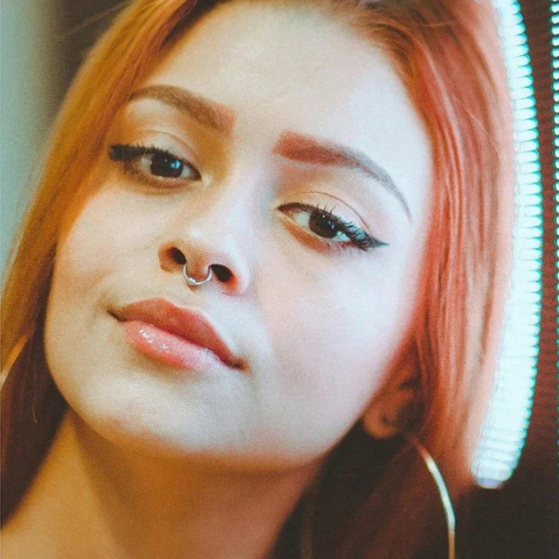 Close-up portrait of a woman with reddish hair wearing a nose ring and septum ring.