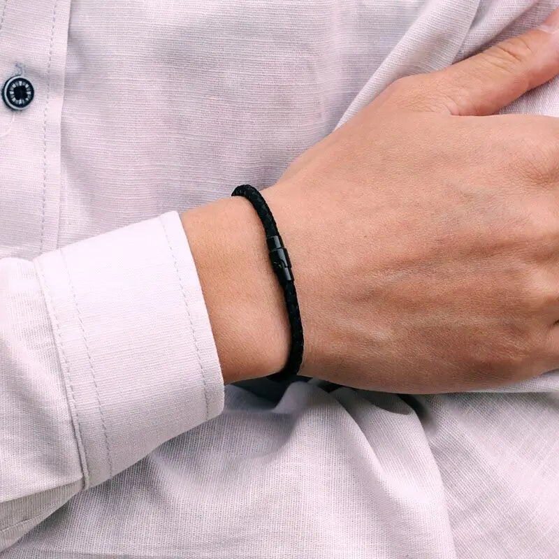 A close-up of a hand wearing a black thread charm bracelet on a light pink shirt sleeve.