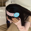 A person is wearing a vintage polka dot button headband on their dark hair while resting in bed.
