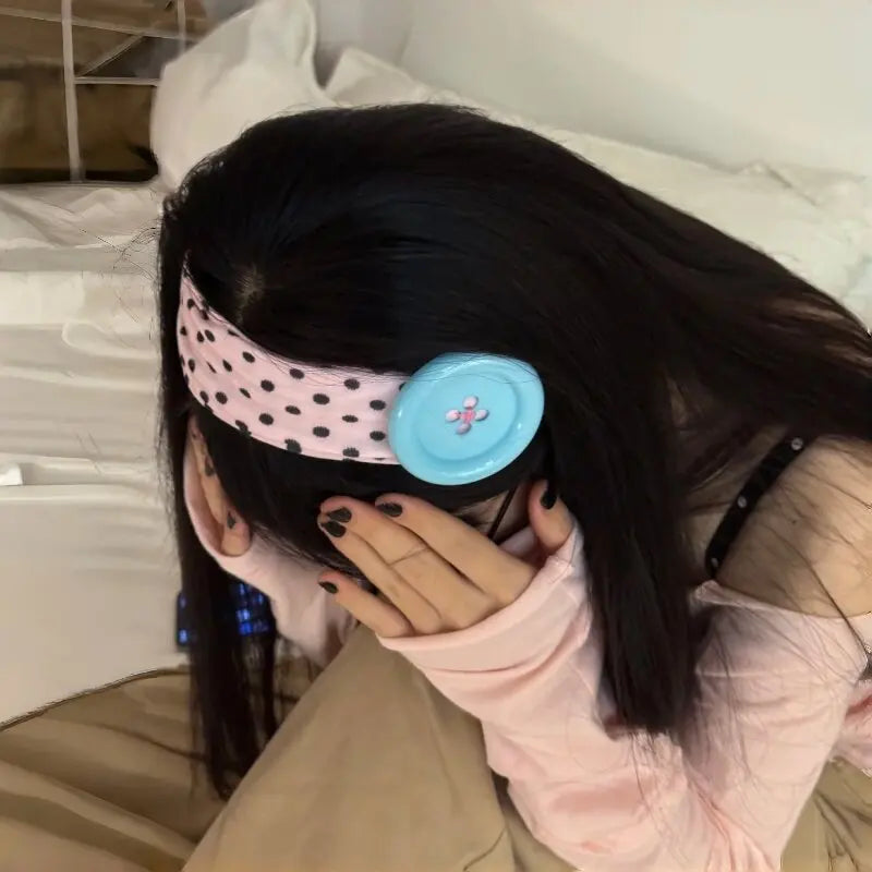 A person is wearing a vintage polka dot button headband on their dark hair while resting in bed.
