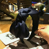 A dark navy blue chic wide bow headband is displayed on a wooden surface.