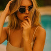 Blonde Frau mit retro ovalen 90er Cat-Eye-Sonnenbrille bei einem Pool im Freien.