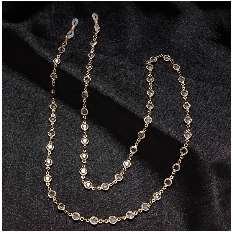 سلسال حجر لؤلؤ بلون ذهبي للنظارات معروض على خلفية قماش داكنة.