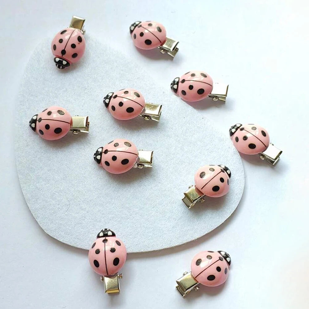 A set of ten pink ladybug hair clips with gold-toned findings arranged on a white surface.