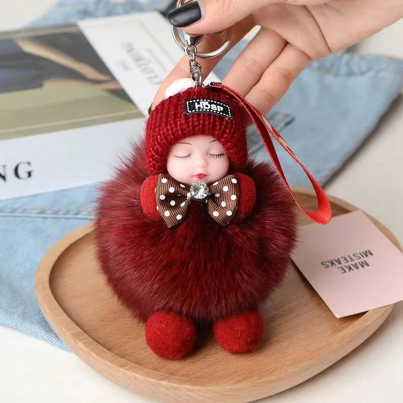 A small, fuzzy red plush doll with a knitted hat and bow is held by a hand against a wooden surface.