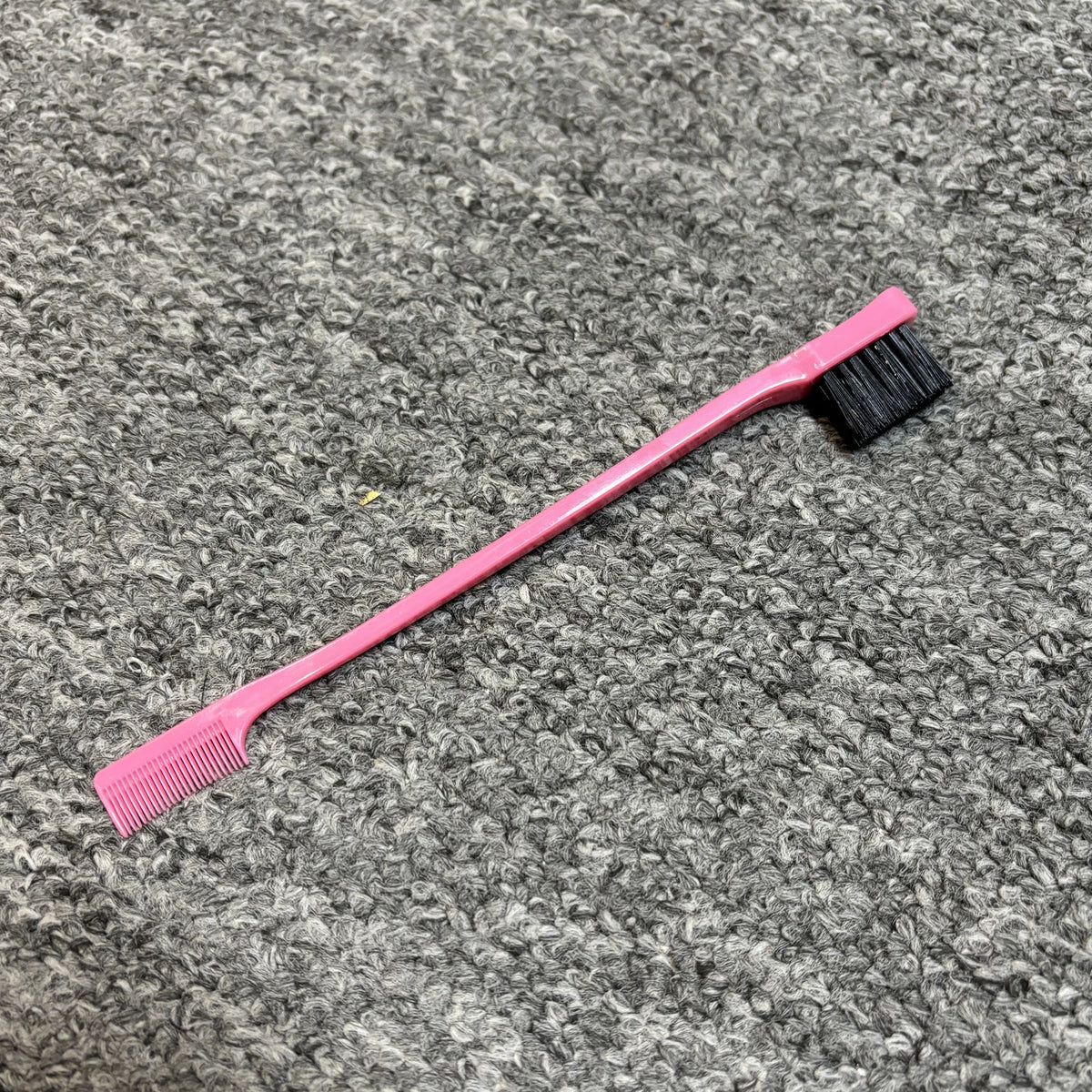 Rosa professionelle doppelseitige Augenbrauenbürste mit schwarzem Pinsel auf grauem strukturiertem Untergrund