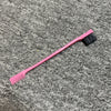Rosa, doppelseitige Augenbrauenbürste mit schwarzem Pinsel auf grauer, strukturierter Oberfläche.