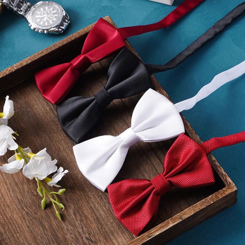 Une collection de nœuds papillons rouges, noirs et blancs arrangés dans un plateau en bois.