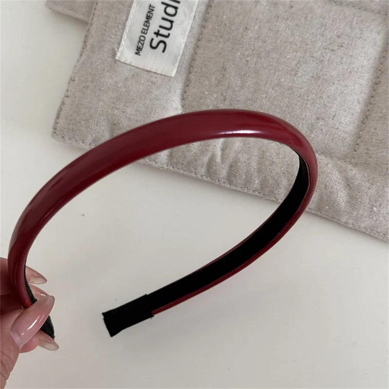 A maroon PU leather fashion headband is shown resting on a beige cloth with a white label.