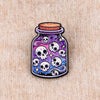 A colorful enamel pin shaped like a glass jar with skulls and stars, featuring purple and blue hues.