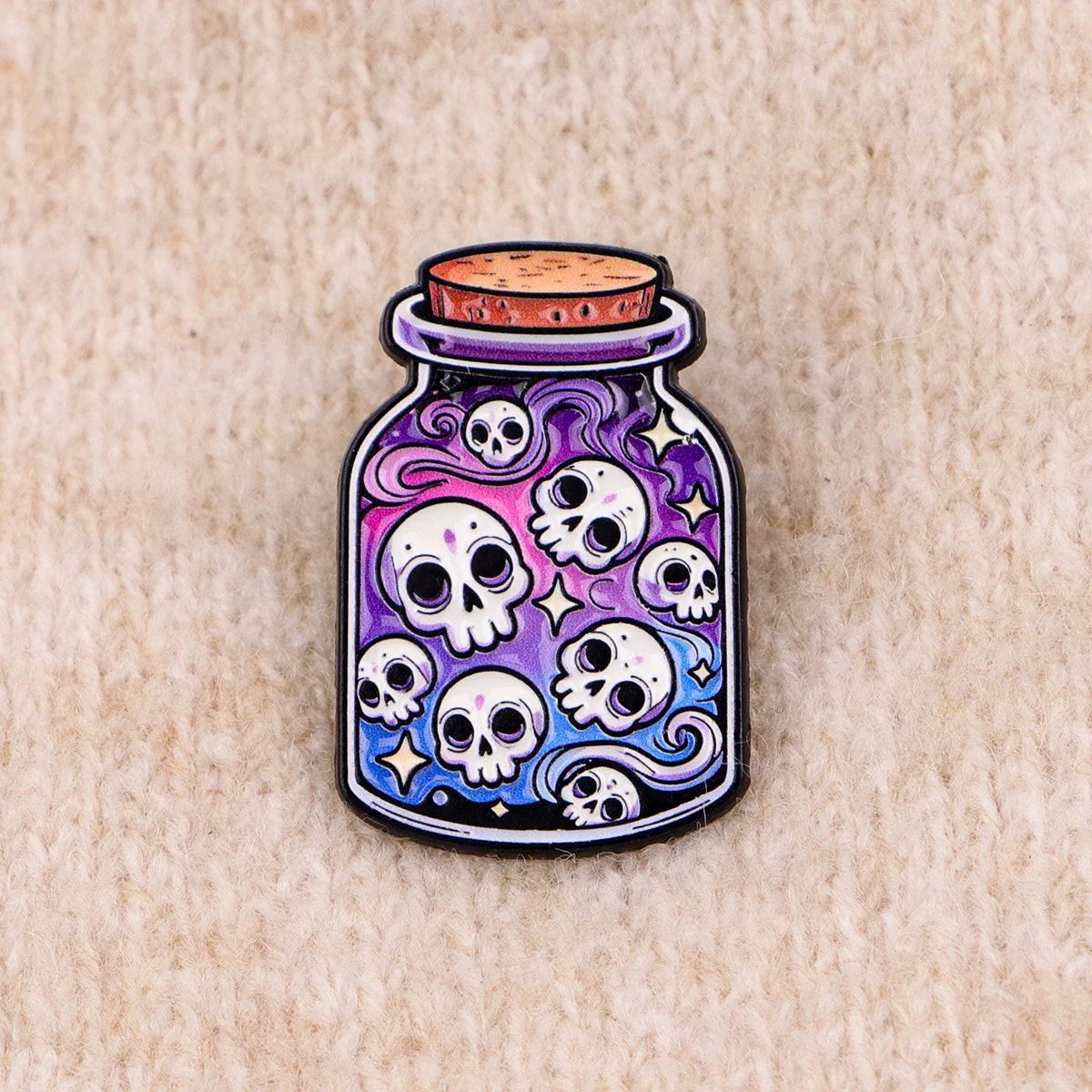 A colorful enamel pin shaped like a glass jar with skulls and stars, featuring purple and blue hues.