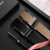 A black smartwatch and leather belt are displayed on a dark surface with a gold pen.