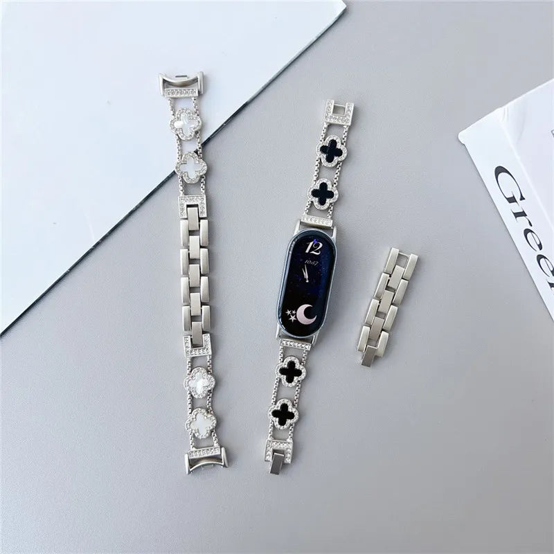 Silver diamond four-leaf clover watch strap for a Xiaomi Mi Band displayed on a gray surface.