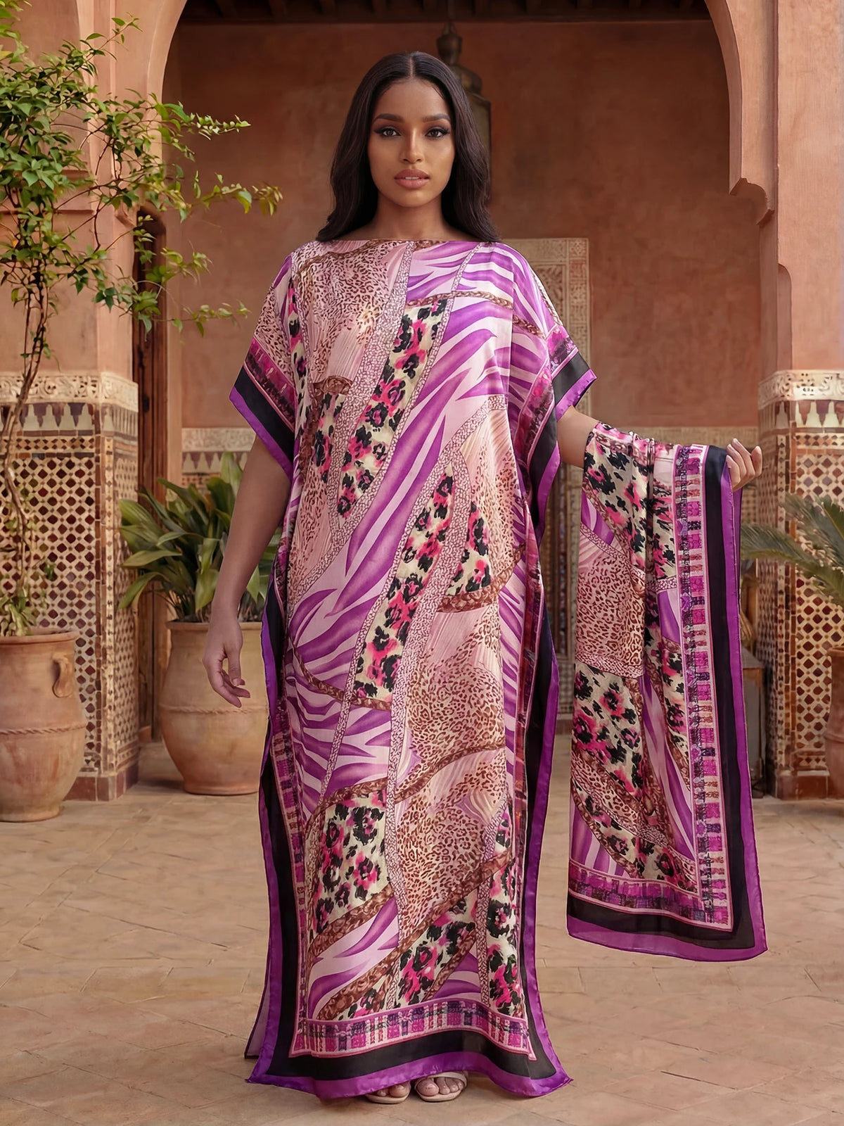 Un mannequin porte une caftan abaya léopard zèbre rose et violet dans un décor architectural terracotta.