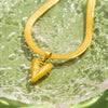 Goldene Schlangenketten-Halskette mit Herzanhänger auf grüner, strukturierter Oberfläche.