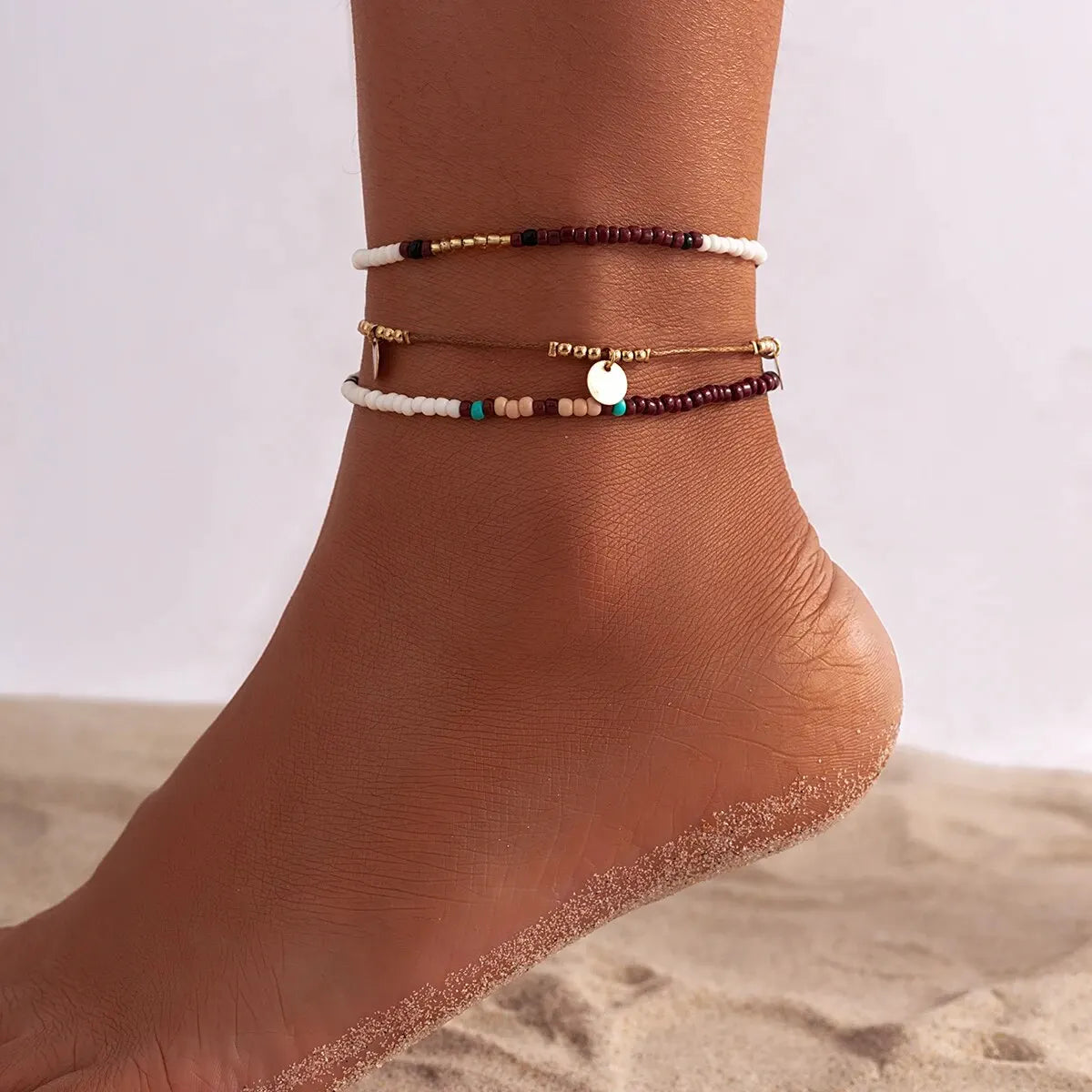 A set of bohemian sequin rice bead anklets worn on a person's ankle.