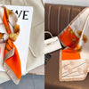 A peach and orange floral print silk scarf draped on a white card against a beige fabric background.