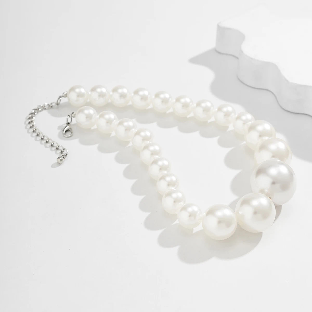 Une guirlande de perles blanches imitations formant un collier ras-de-cou est présentée sur fond blanc.