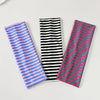Trois élastiques pour cheveux à rayures bleues, noires et roses disposés sur une surface blanche.