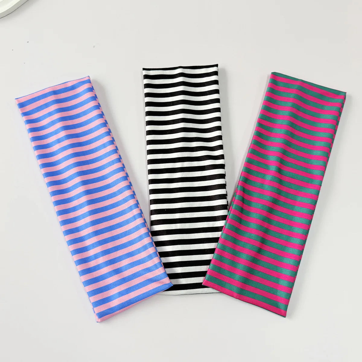 Trois élastiques pour cheveux à rayures bleues, noires et roses disposés sur une surface blanche.