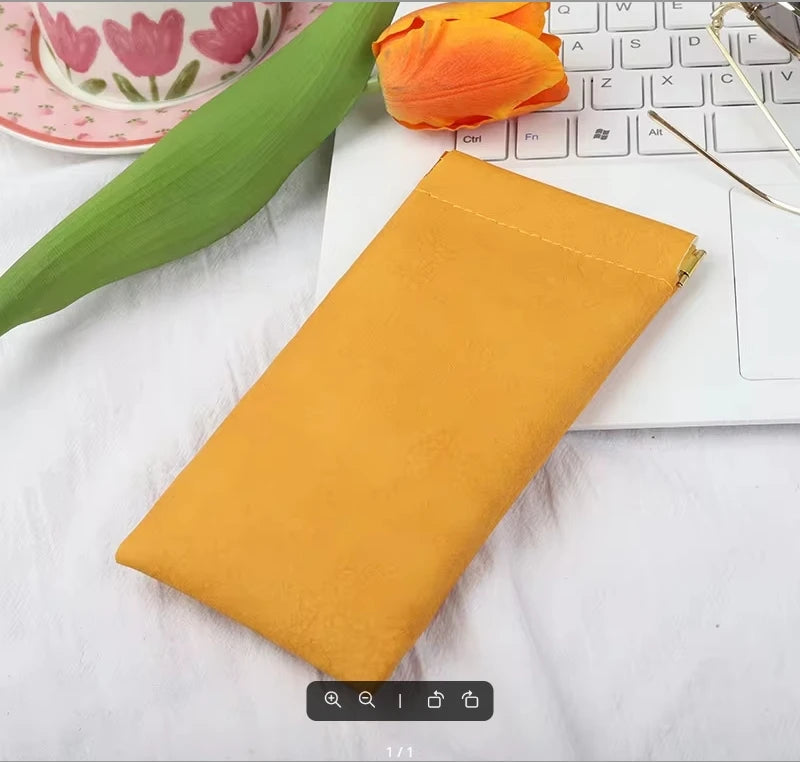 A yellow premium PU leather storage bag resting on a white surface next to a laptop and an orange flower.