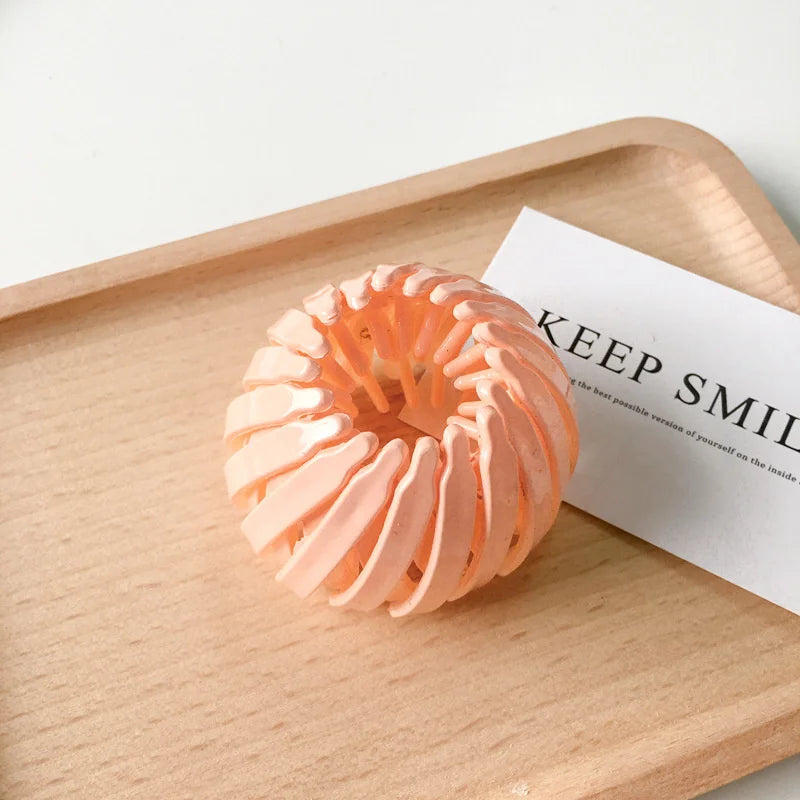 A close-up of an elegant orange silicone horsetail hair clip resting on a wooden tray next to a card.