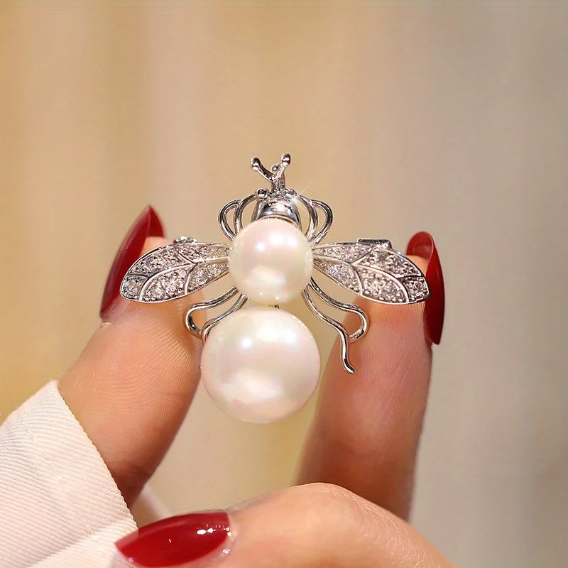 Broche argentée avec motif abeille baroque et accents de perles sur un doigt.