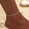 A close-up of a sparkling zircon heart cross anklet worn on a person's ankle.