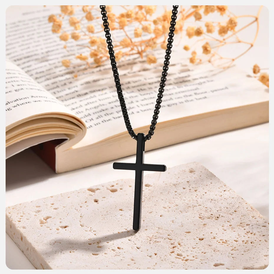 Un collar de cruz de acero inoxidable negro descansa sobre una piedra de color claro junto a un libro abierto con flores seca