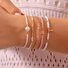 A hand is wearing a stack of delicate pearl and pink beaded bracelets on a wrist.
