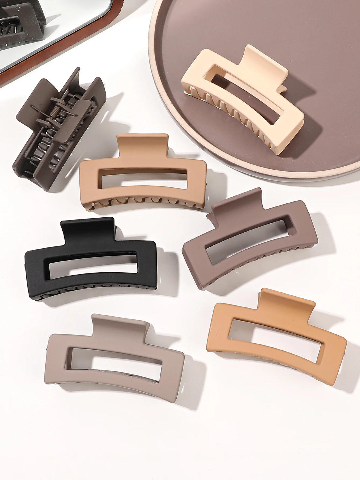 A set of seven square hair claw clips in various neutral tones including beige, taupe, and black, displayed on a light backgr