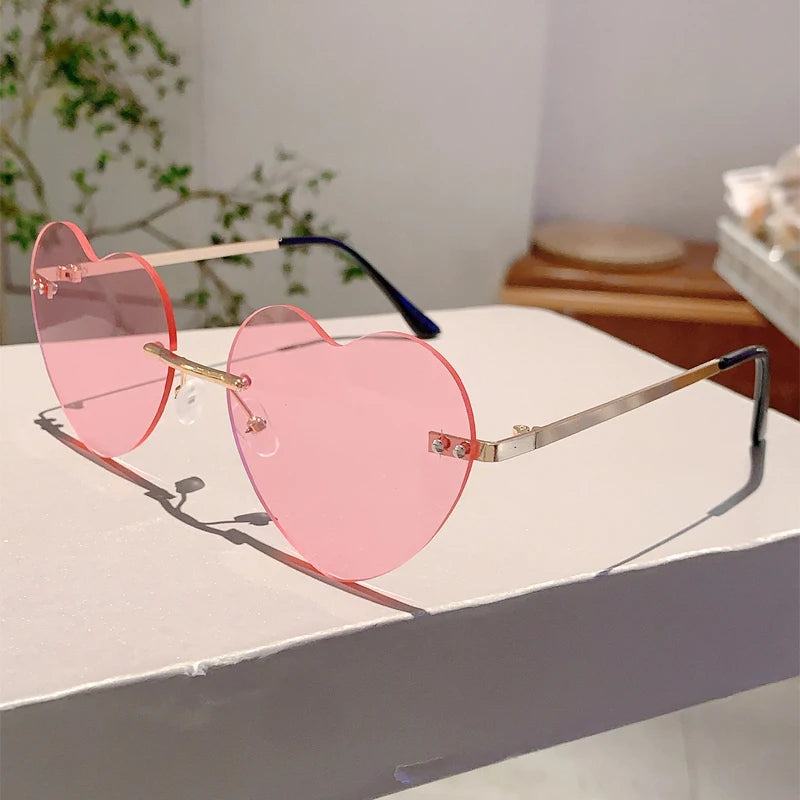 Rosa herzförmige, randlose Sonnenbrille mit gold- und schwarzen Akzenten auf weißem Untergrund.